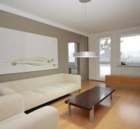 A bright living room in a three-room apartment with wood-patterned flooring and a large sofa.