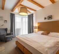 A bedroom in a 3-room apartment with wooden beams and a comfortable chair by the bed.