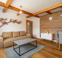 A bright living room in a three-room apartment with a wooden decor floor and wooden beams.
