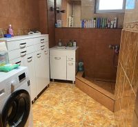 A bathroom with white cabinets, a washing machine, and a shower in a family house.