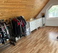 An attic room in a family house with clothing and a dresser, wooden decor flooring.