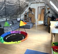 Attic playroom in a family house with a swing, sofa, and wooden decor flooring.
