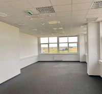 Office spaces with carpet flooring and a large window in a warehouse and hall building.