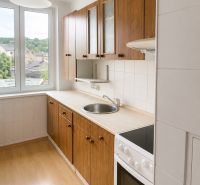 The kitchen of a 3-room apartment with a door to the balcony and a floor with a wooden decor.