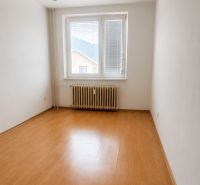 An empty room in a three-room apartment with a wooden patterned floor and a radiator.
