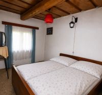 A cottage with a cozy bedroom, wooden ceiling, and a retro TV on a table.