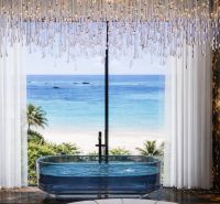 A glass bathtub with a view of the beach from a 5 or more room apartment.