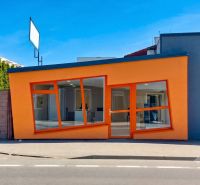The orange facade of commercial spaces on Zlatovska Street in Trenčín with large glass windows.