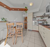 A kitchen in a 4-room apartment with a stove, a bar counter, and wooden chairs.