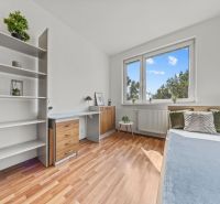 A room in a 4-room apartment with a wooden decor floor, a desk, and a bed.