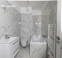 A bathroom with white tiles, a bathtub, and a sink in a 2-room apartment.