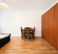 A room in a family house with a wooden floor decor, a bed, a wardrobe, and a dining table.