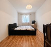 Bedroom in a family house with a bed, television, and wooden decor flooring.