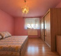 A bedroom with pink walls, a bed, and a wardrobe, with a wooden decor floor.