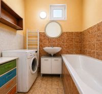 A bathroom with a bathtub, a washing machine, and a colorful dresser in a family house.