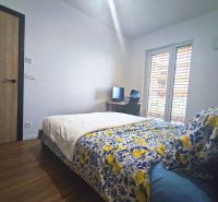 Bedroom in a 2-room apartment with a bed, wood-patterned floor, and a desk.