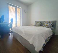 A bedroom in a two-room apartment with a wooden decor floor and a bed by the window.