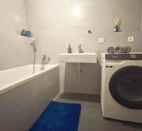 Bathroom in a 2-room apartment with a bathtub, sink, and washing machine on a tiled floor.