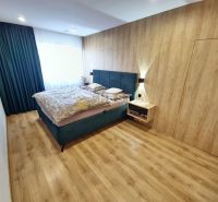Bedroom in a family house with a bed, a headboard wall with wooden decor, and flooring.