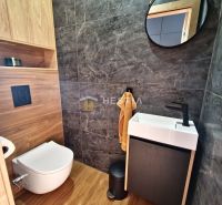 A bathroom in a family house, with a sink, a mirror, and a floor with a wooden decor.
