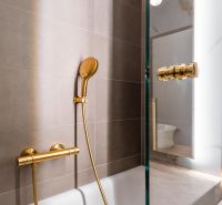A bathroom with a bronze shower and neutral tiles in a 3-room apartment.