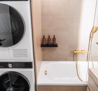 A bathroom in a three-room apartment with a bathtub, a washing machine, and decorative bottles on the shelf.