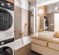 A bathroom in a 3-room apartment with a bathtub, sink, dryer, and elegant gold accessories.