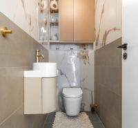 A toilet with a sink, a gold faucet, and marble-patterned tiles in a three-room apartment.