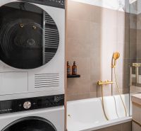 A bathroom in a 3-room apartment with a washing machine, dryer, bathtub, and gold accessories.