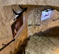 A stone staircase in a building with decorative light fixtures and female portraits on the walls.