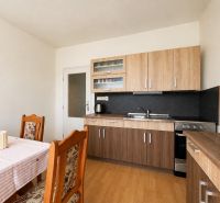 A kitchen in a studio apartment with wooden furniture and flooring, dining table.