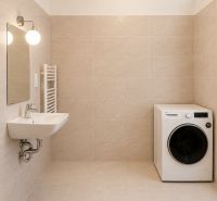 Bathroom in a 2-room apartment with a washing machine and a sink on light tiles.