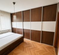 Bedroom with a sliding wardrobe, bed, and wooden decor flooring in a 2-room apartment.