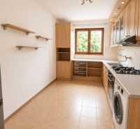 A kitchen in a 2-room apartment with wooden cabinets, appliances, and a window.