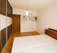 Bedroom in a 2-room apartment with a wood-patterned floor and a built-in wardrobe.