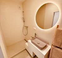 A bathroom in a 3-room apartment with a large illuminated mirror and a shower without a door.