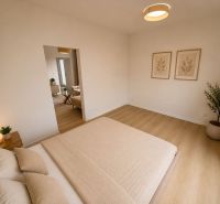 A bright bedroom with a bed, decorations, and a wood-patterned floor in a three-room apartment.