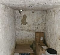 Storage space in a cabin with various boxes and plastic barrels on the floor.