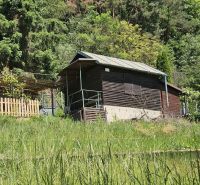 A cottage in Budatín on the edge of the forest, surrounded by greenery and a wooden fence.