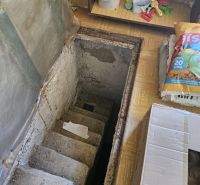 Concrete stairs in the cottage leading to the basement, surrounded by stored items.