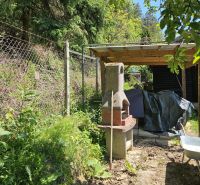 A garden fireplace next to a cottage on a forest road in Budatín surrounded by greenery.