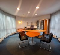 An office with a wooden decor desk, shelves, and illuminated vertical blinds.