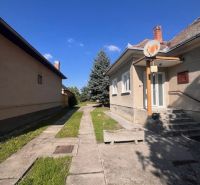 The exterior of a family house in Vrakúň, a sidewalk, a lawn, a tree, and a blue sky.