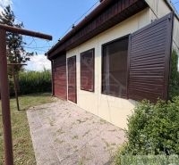 A cottage in Nové Zámky with closed wooden shutters and surrounding greenery in the garden.