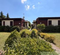 A cottage in Nové Zámky surrounded by a landscaped garden and greenery, blue sky.