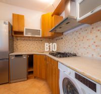 A kitchen with a tiled wall, appliances, and a wooden decor floor in a two-room apartment.