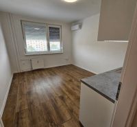 A studio apartment with a wooden decor floor, air conditioning, and a large window for light.