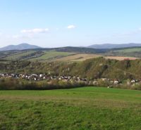 A view of agricultural and forest lands in Bogliarka with a hilly horizon and a village.