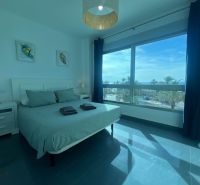 Bedroom of a holiday apartment with a large window, bed, and tables.