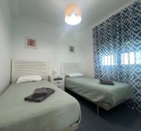 Recreational apartment with two single beds, patterned curtains, and a table with a lamp.